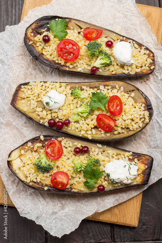 Halves of baked eggplant with bulgur and tomatoes on cutting board.