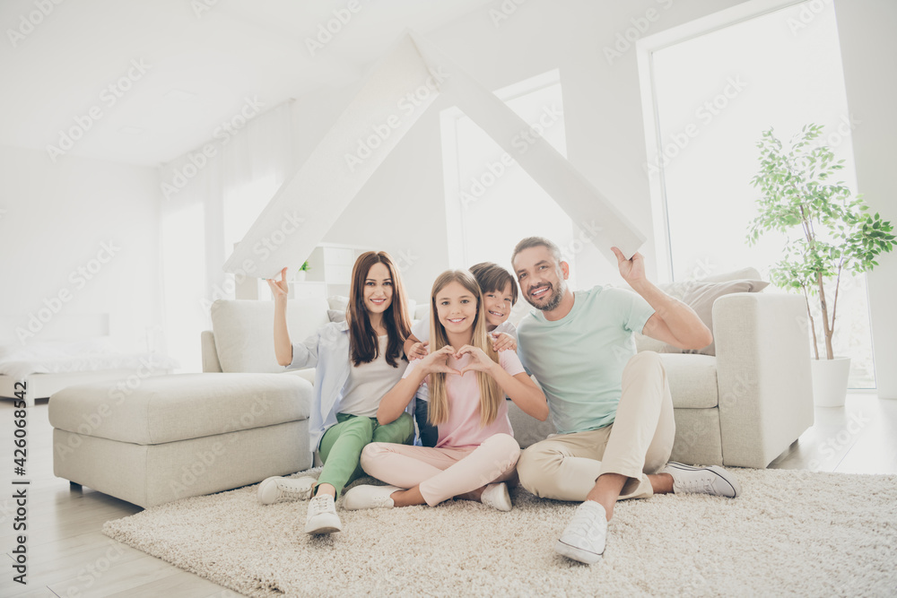 Full size photo of optimistic family mom dad two kids show home heart sit on floor wear t-shirts trousers at home Full size photo of optimistic family mom dad two kids show home heart sit on floor wear t-shirts trousers at home