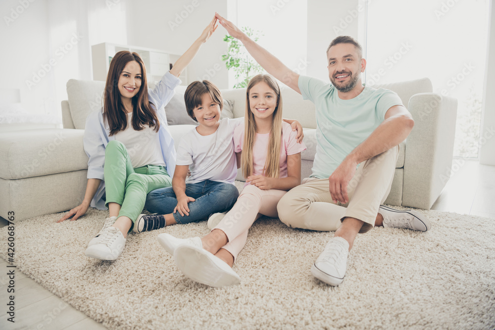 Full size photo of optimistic family mom dad two kids show home sit on floor wear t-shirts trousers at home Full size photo of optimistic family mom dad two kids show home sit on floor wear t-shirts trousers at home