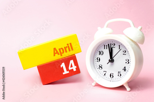 April 14th. Day 14 of month, Calendar date.White alarm clock on pastel pink background. Spring month, day of the year concept.
