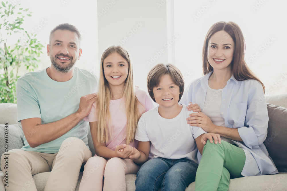 Photo of optimistic full family with two kids hug sit on sofa wear casual cloth t-shirts pants at home Photo of optimistic full family with two kids hug sit on sofa wear casual cloth t-shirts pants at home