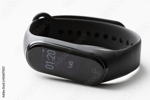 Black fitness watch or activity tracker with time and steps on display. Fitness tracker lies on white background. Closeup, selective focus