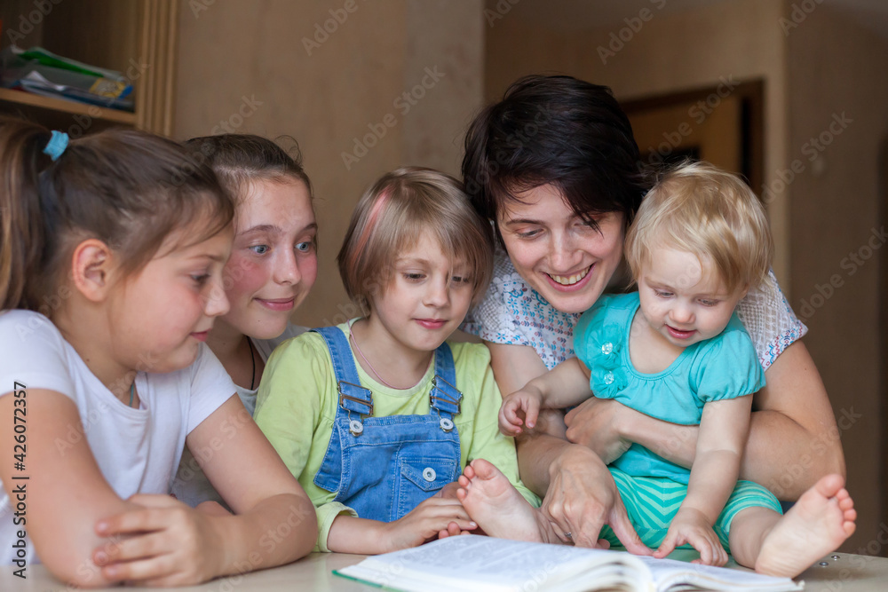 Children read book at table with their mother Children read book at table with their mother