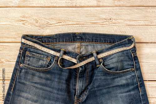 Measuring tape for weight loss in jeans on a wooden background. The concept of being overweight. Selective focus.