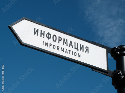 Text in Russian and English - Information. Tourist Information sign on the arrow, pointer against the blue sky. 