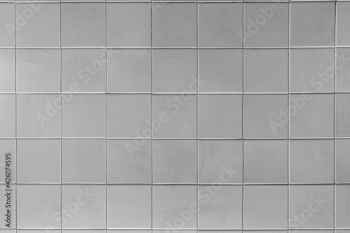 The texture of light gray square glossy ceramic tiles. Soft lighting.