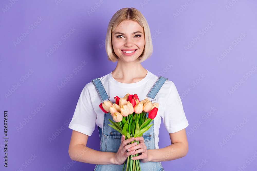 Photo of nice optimistic short hairdo blond lady hold flowers wear white t-shirt isolated on violet background Photo of nice optimistic short hairdo blond lady hold flowers wear white t-shirt isolated on violet background