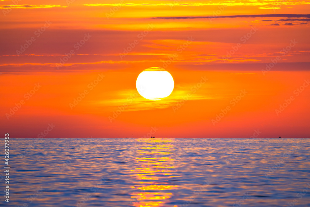 Sun rising in the sea with a fishing boat in the rays of the sun above the waves. Beautiful sunrise on the ocean with a big and colorful sun in summer. A new day begins.