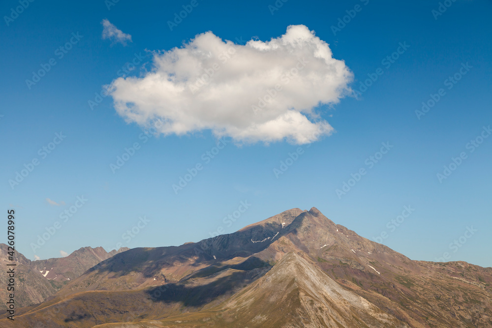 Landscape photography of steep mountains in summer, lonely clouds, and silent high altitude pastures, in the Aragonese Pyrenees, Huesca province, in the area of the Posets-Maladeta Natural Park.