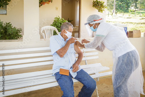 Obraz na plátně Elderly man receives vaccine against Covid 19 on the veranda of her house, in a