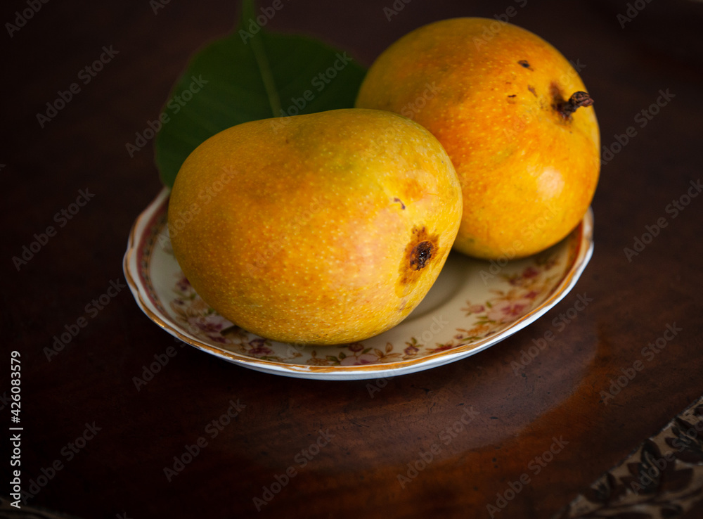 Two ripe Alphonso mango's on a ornate plate on an ornate wooden, walnut, table, decorative