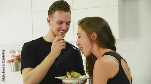 Man and woman couple in casual outfit eating and feeding his girlfriend for healthy food salad for self care in modern kitchen