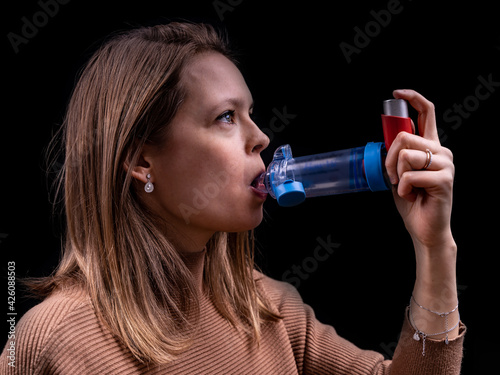 Young women taking asthma medication with an inhaler and spacer with a black background