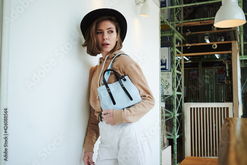 A girl with a blue bag looks out the window where she stands in a cafe