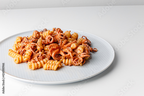 Fresh italian pasta with baby octopus. Close up of calamarata octopus italian traditional sicilian pasta homemade seafood sauce with tomato,basil,parsley,herbs,chilly. photo