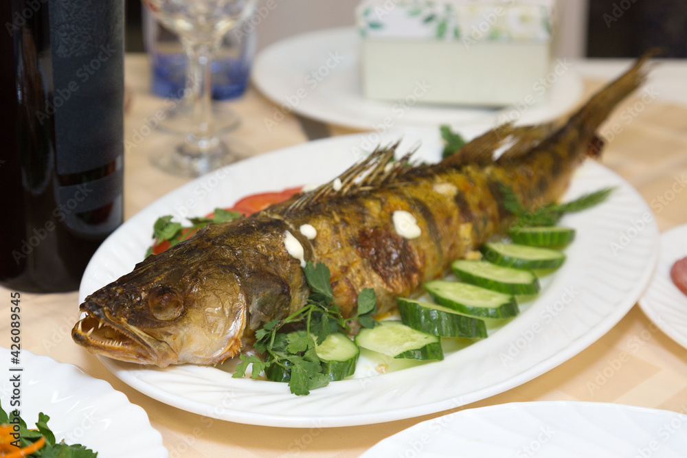 Large fried fish on a platter with vegetables and herbs. Large fried fish on a platter with vegetables and herbs.