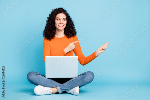 Portrait of attractive cheerful girl sitting in lotus pose using laptop demonstrating copy space isolated over bright blue color background © deagreez