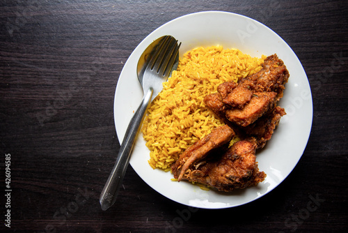 Top view Muslim yellow rice with fried chicken in white dish on light brown wooden background. Halal Food in Thailand. simply and local food.