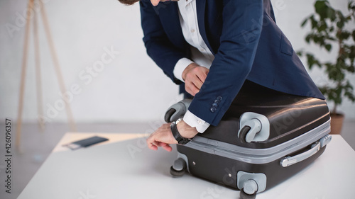 cropped view of businessman in suit zipping luggage