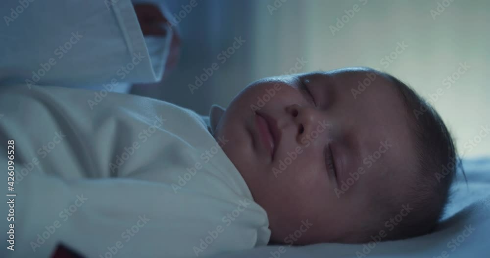 Cinematic macro shot of new mother is caressing and kissing with affection her newborn baby while is sleeping peacefully with sweet dreams in a crib with soft blanket in a nursery at night. Cinematic macro shot of new mother is caressing and kissing with affection her newborn baby while is sleeping peacefully with sweet dreams in a crib with soft blanket in a nursery at night.
