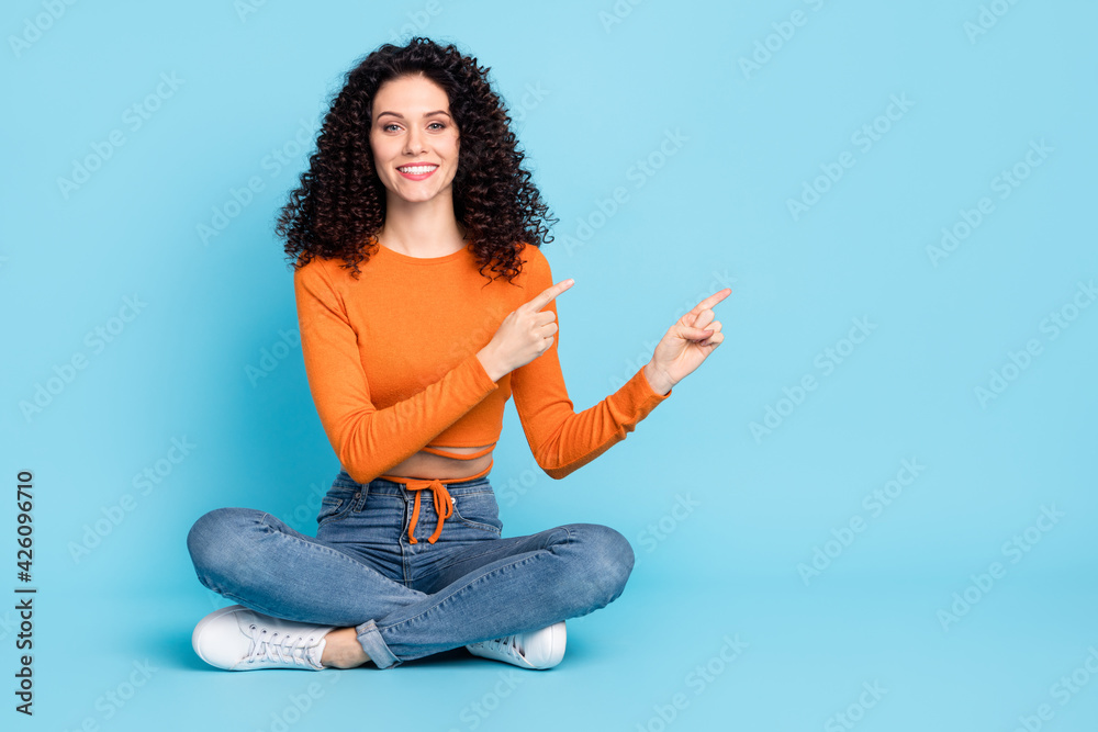 Full length body size photo of curly girl pointing fingers on empty space advising isolated on bright blue color background Full length body size photo of curly girl pointing fingers on empty space advising isolated on bright blue color background