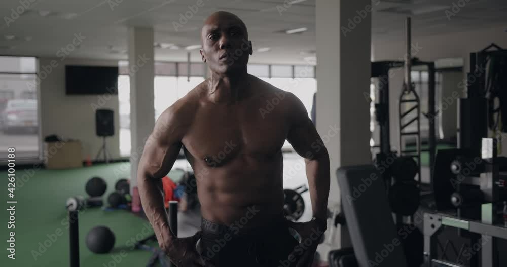 Black man with six pack abs turns and makes eye contact with camera in gym