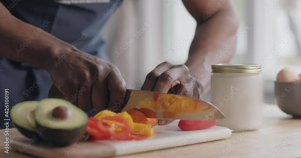 Closeup, Hands of black man chopping peppers on cutting board by avocado Closeup, Hands of black man chopping peppers on cutting board by avocado