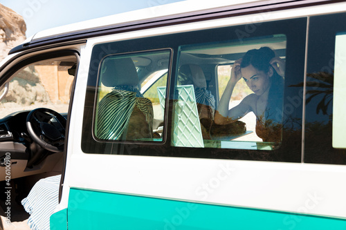 Attractive woman in a bikini, looks at herself in a mirror while combing her hair inside her camper van, road trip concept