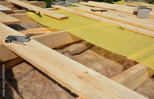Roofing construction: A close-up of a vapor barrier, membrane installation on a roof with a staple gun over mineral wool, mineral glass insulation. © bildlove
