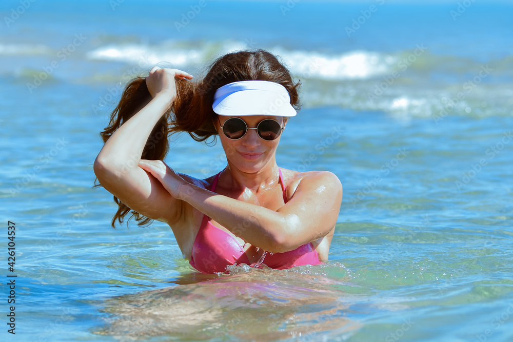 woman wearing glasses and a sun visor holding her hair while enjoying the sea waters