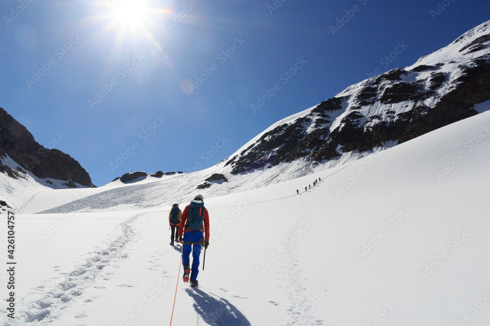 Rope team mountaineering with crampons on glacier Sexegertenferner towards Sexegertenspitze and mountain snow panorama with blue sky in Tyrol Alps, Austria