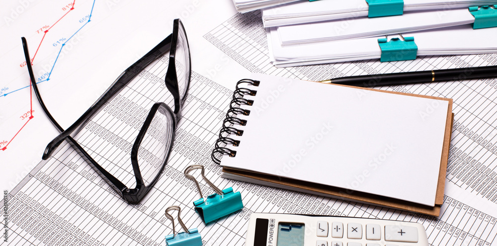 On the desktop are glasses, paper clips, a blank notebook and a pen. Business concept