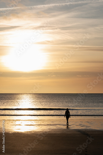 A silhouette of a woman walking on a black beach during sunset. The photo is taken in Akranes in Iceland where swimming in the sea is popular all year around.