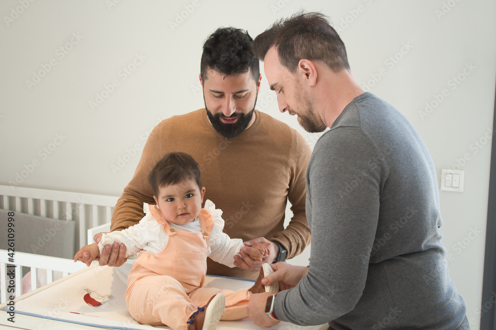 Gay married couple changing their daughter´s diaper in the bedroom. Gay married couple changing their daughter´s diaper in the bedroom.