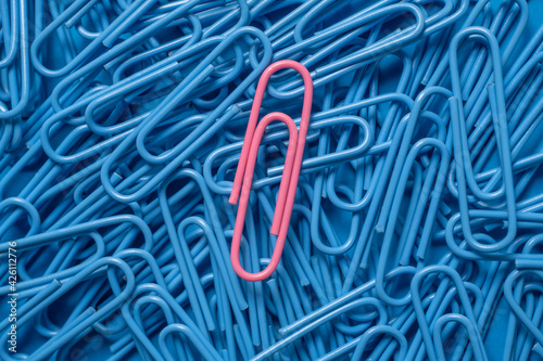 Pink paper clip on pile of blue paper clips