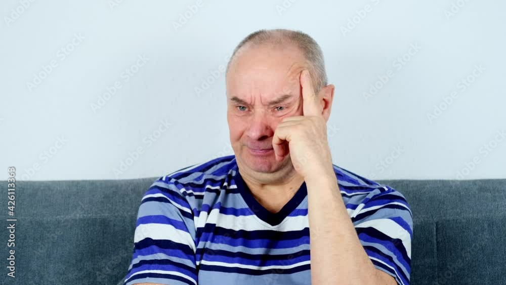 adult bald man in striped t-shirt sits on the couch and watching tv, looks closely, concept of hobbies and free time, rest at home adult bald man in striped t-shirt sits on the couch and watching tv, looks closely, concept of hobbies and free time, rest at home