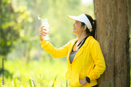 Healthy athletic woman drinking pure water after go running to be fresh in the nature park. Asian runner woman after exercise. Healthy and Lifestyle concept. On Nature background