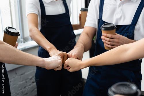 Cropped view of workers of cleaning company with coffee to go doing fists bump in office