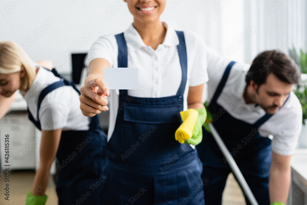 Empty card in hand of african american cleaner near colleagues in office Empty card in hand of african american cleaner near colleagues in office