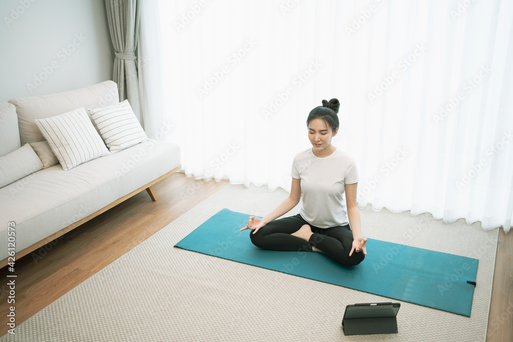 Portrait of gorgeous young asian woman practicing yoga at home stretching out while following a yoga routine. Portrait of gorgeous young asian woman practicing yoga at home stretching out while following a yoga routine.