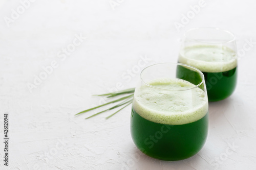 Wheatgrass juice in a glass on a white concrete background
