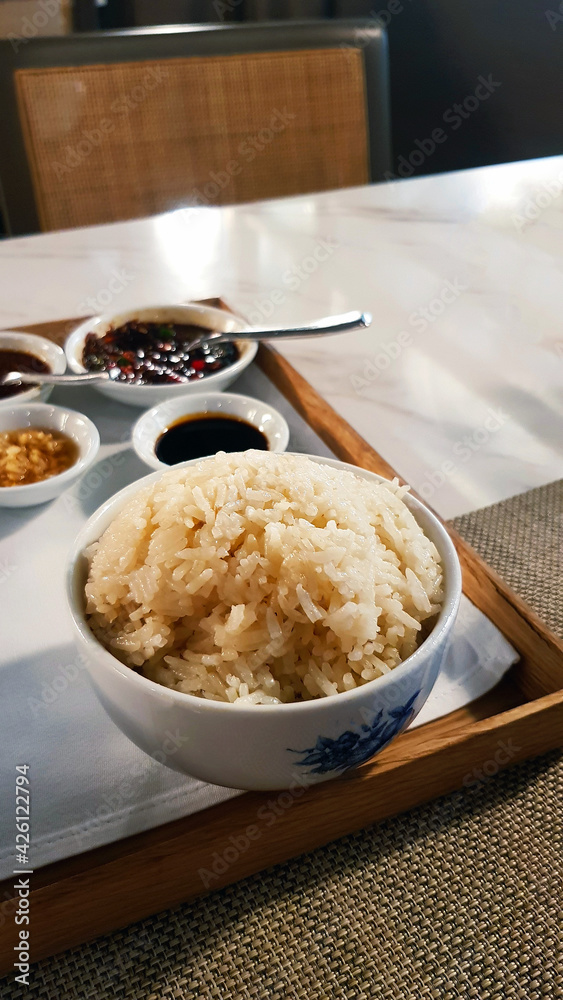 Close up oily rice with blurred sweet, spicy and salt sauce for eat with boiled chicken in Thai or Singapore style on wooden tray on table. Asian food concept. Close up oily rice with blurred sweet, spicy and salt sauce for eat with boiled chicken in Thai or Singapore style on wooden tray on table. Asian food concept.