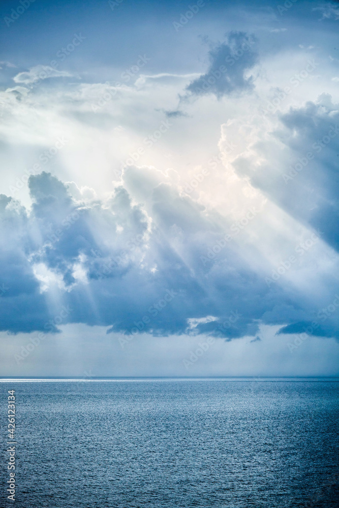 Sunbeam rays shining through the clouds on blue sky over the ocean Sunbeam rays shining through the clouds on blue sky over the ocean