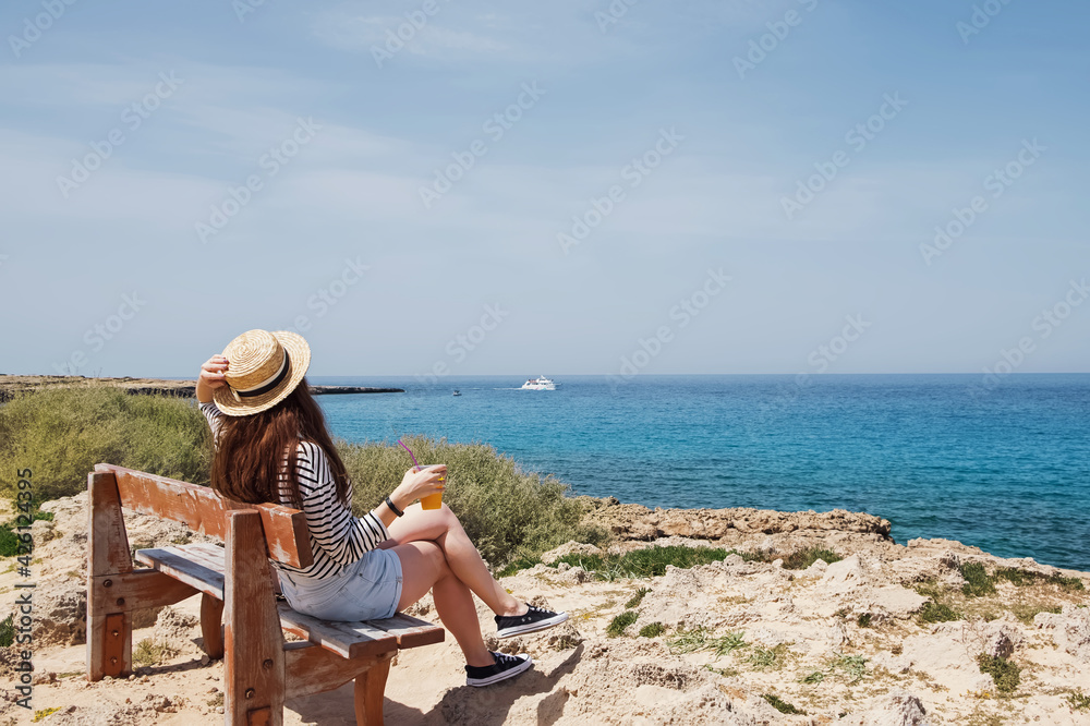 Woman in straw hat sitting on the bench near the sea.