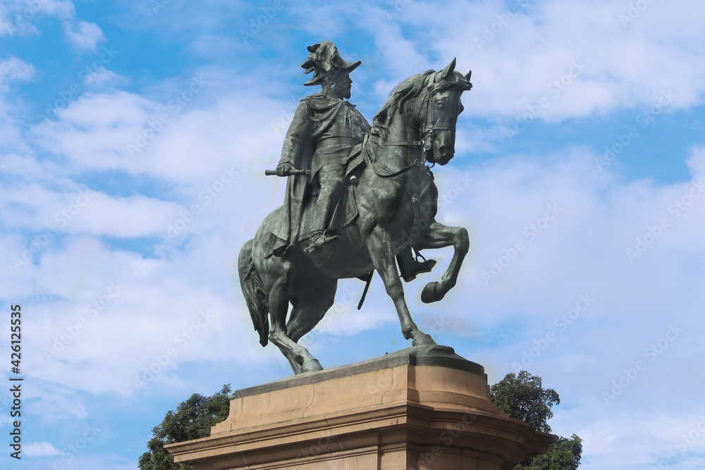 A bronze statue of King Edward VII in uniform on horseback. The statue is on a sandstone plinth. Blue sky background
