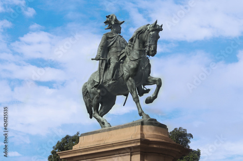 A bronze statue of King Edward VII in uniform on horseback. The statue is on a sandstone plinth. Blue sky background