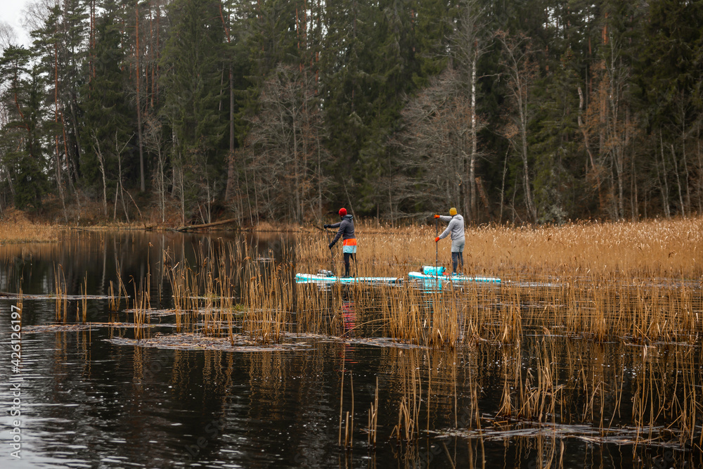 Obraz premium Two guys paddle with SUP or stand up paddle board in small river. concept of harmony with the nature. Stand up paddle boarding - awesome active outdoor recreation.