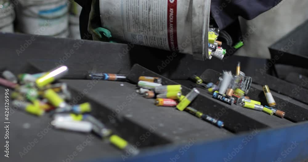 View of hands of person in uniform and gloves pouring out used batteries from bucket onto a moving conveyor belt, for separation and recycling. Processing. Environmental protection concept.