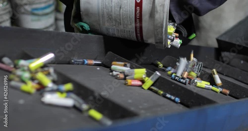 View of hands of person in uniform and gloves pouring out used batteries from bucket onto a moving conveyor belt, for separation and recycling. Processing. Environmental protection concept.