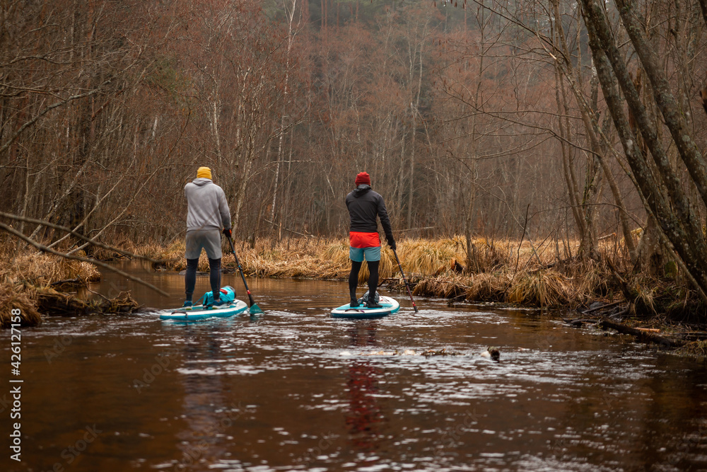 Two guys paddle with SUP or stand up paddle board in small river. concept of harmony with the nature. Stand up paddle boarding - awesome active outdoor recreation.